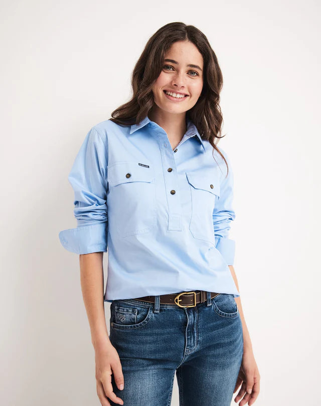 Woman wearing an RB Sellars half button light blue shirt and jeans on a plain background