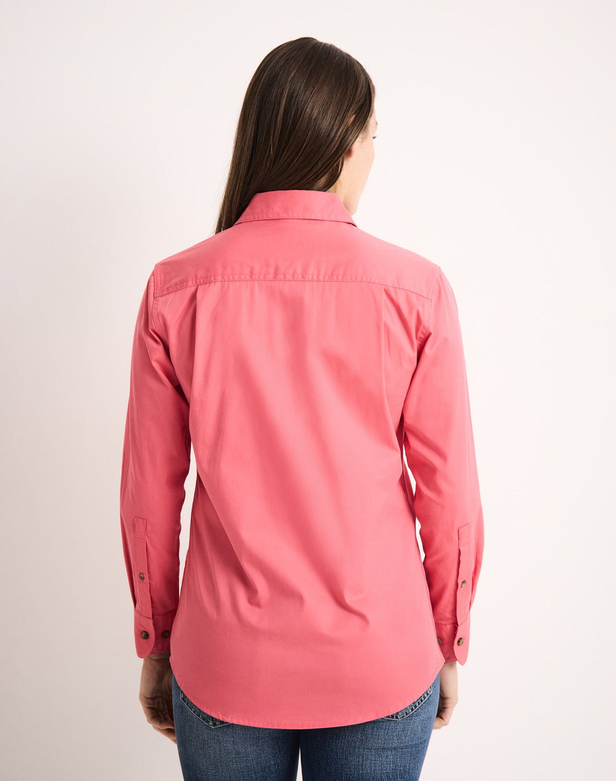 Woman wearing a coral pink work shirt on a plain background