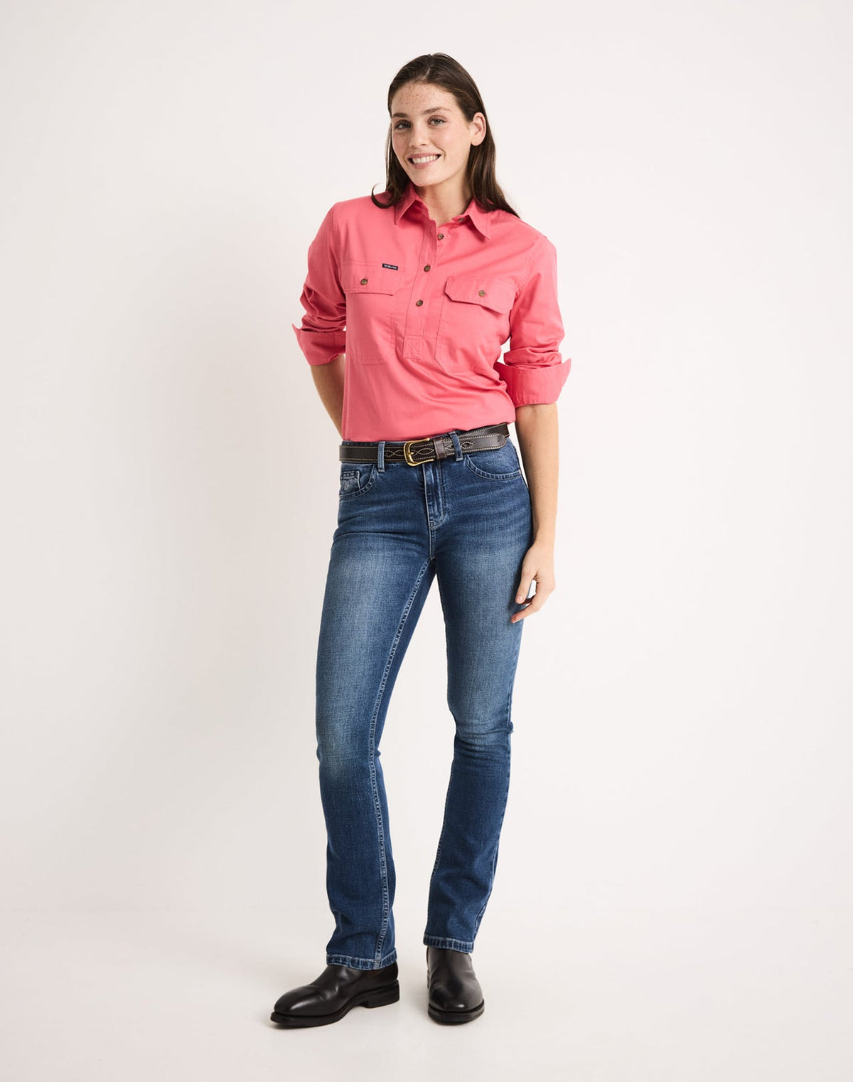 Woman wearing a coral pink RB Sellars shirt and blue jeans on a white background